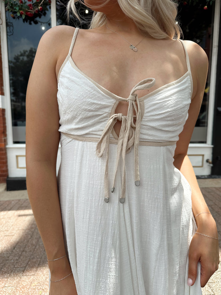 Woman wearing white flowy maxi dress with tan trim detailing. 