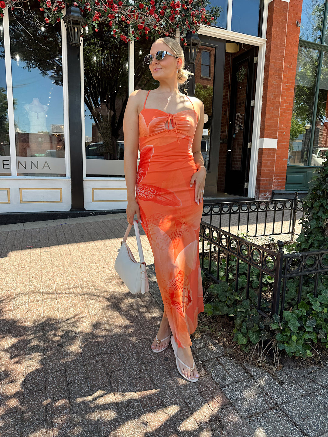 Woman wearing orange floral mesh maxi dress with criss-cross open back with adjustable spaghetti straps. 