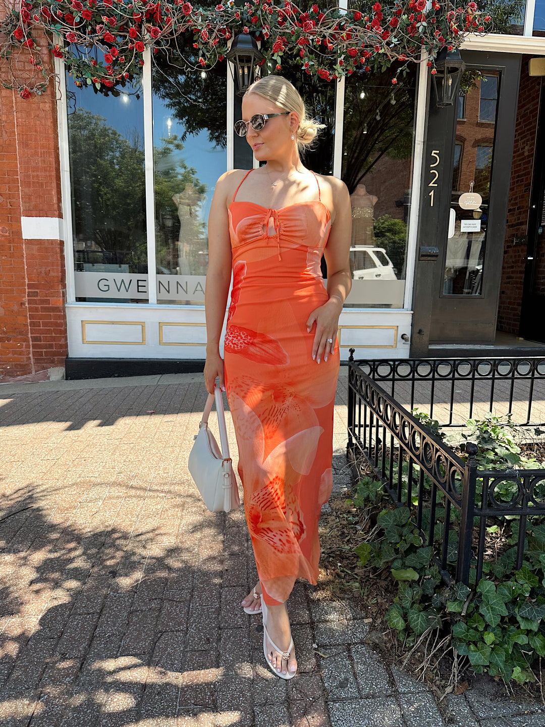 Woman wearing orange floral mesh maxi dress with criss-cross open back with adjustable spaghetti straps. 
