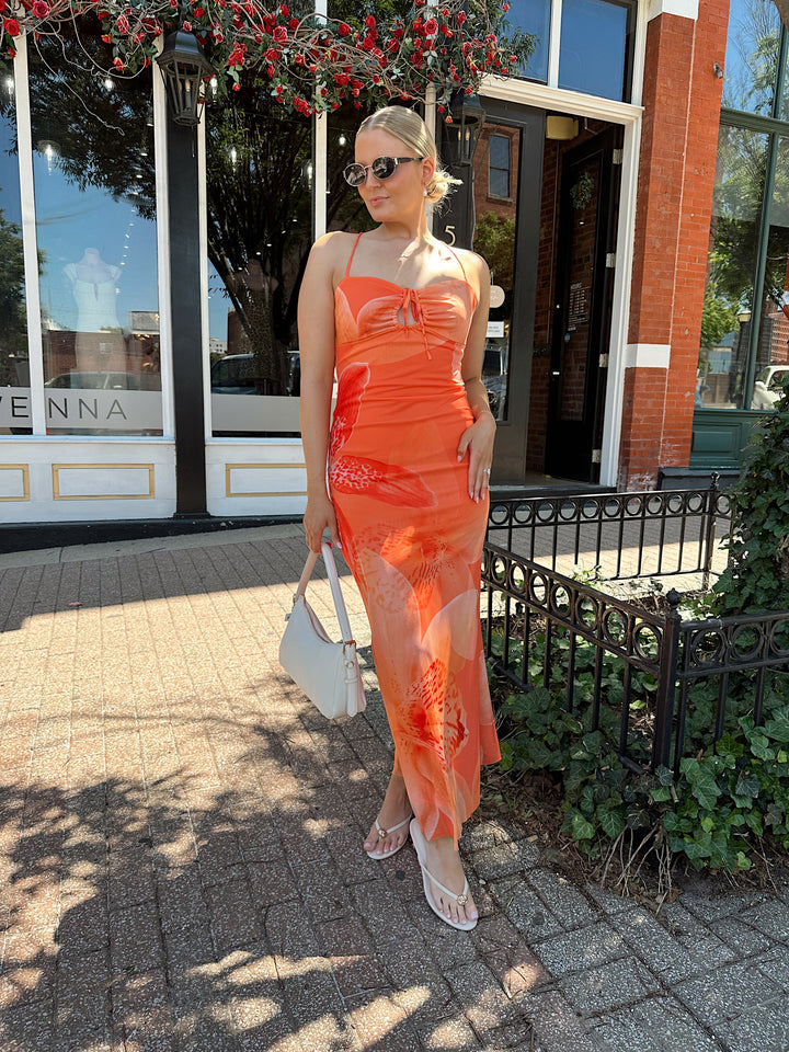 Woman wearing orange floral mesh maxi dress with criss-cross open back with adjustable spaghetti straps. 