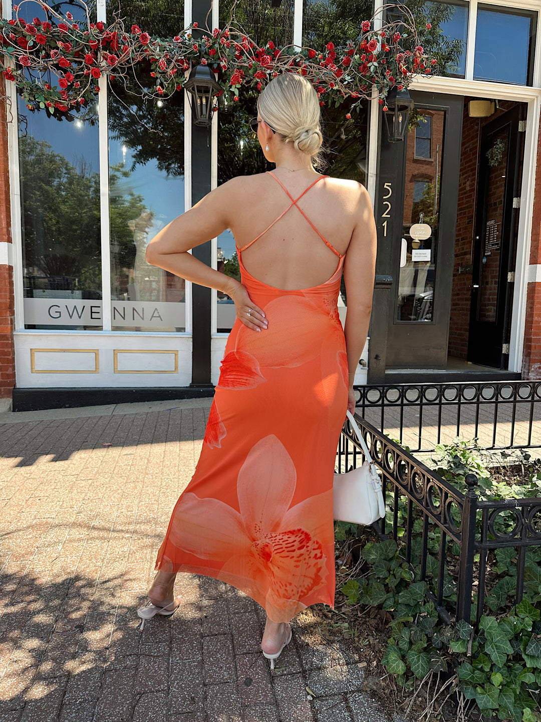 Woman wearing orange floral mesh maxi dress with criss-cross open back with adjustable spaghetti straps. 