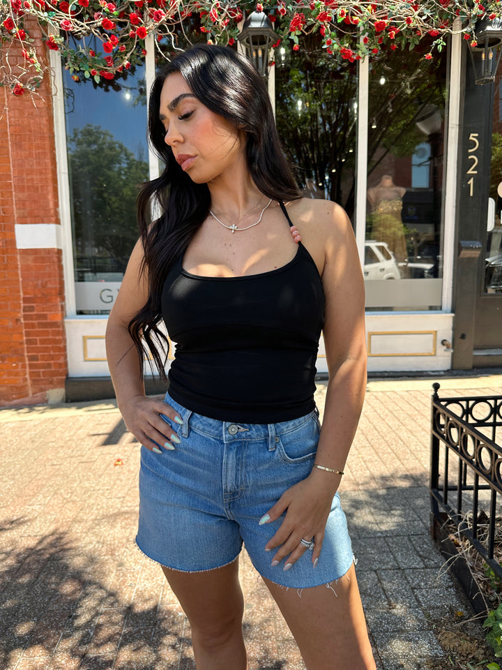 Woman wearing black halter top with beading detail, and denim shorts. 