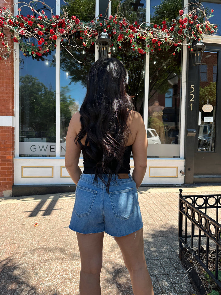 Woman wearing black halter top with beading detail, and denim shorts. 
