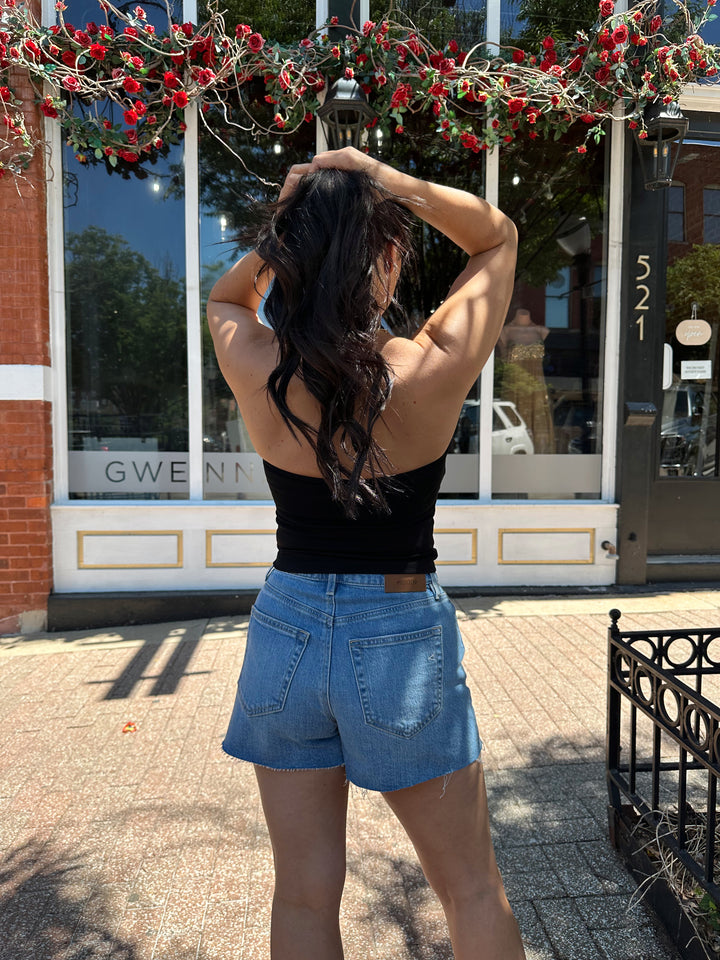 Woman wearing black halter top with beading detail, and denim shorts. 