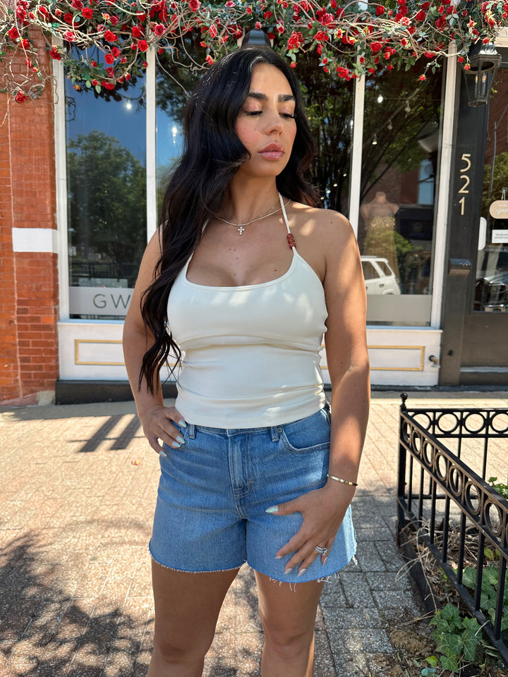 Woman wearing cream colored halter top with beading detail and denim shorts. 