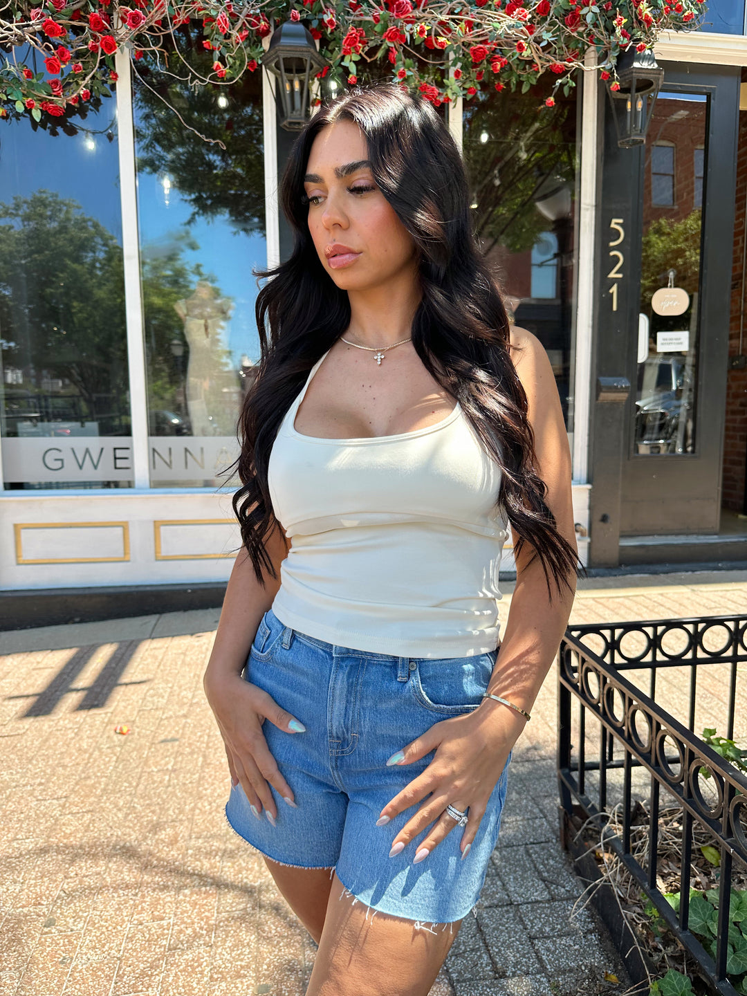 Woman wearing cream colored halter top with beading detail and denim shorts. 