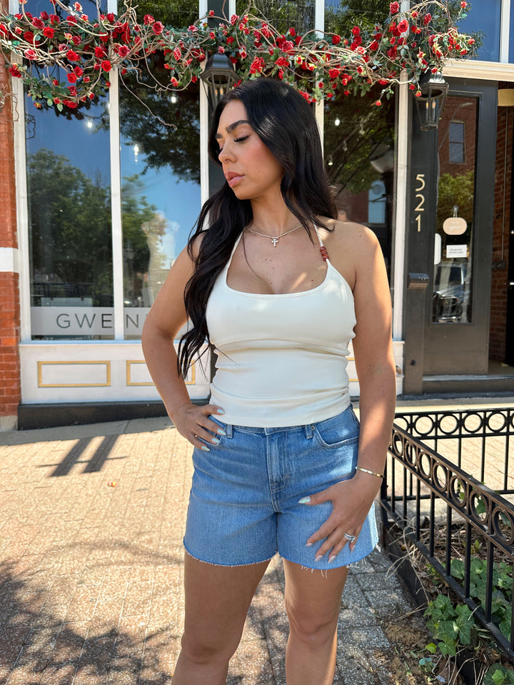 Woman wearing cream colored halter top with beading detail and denim shorts. 