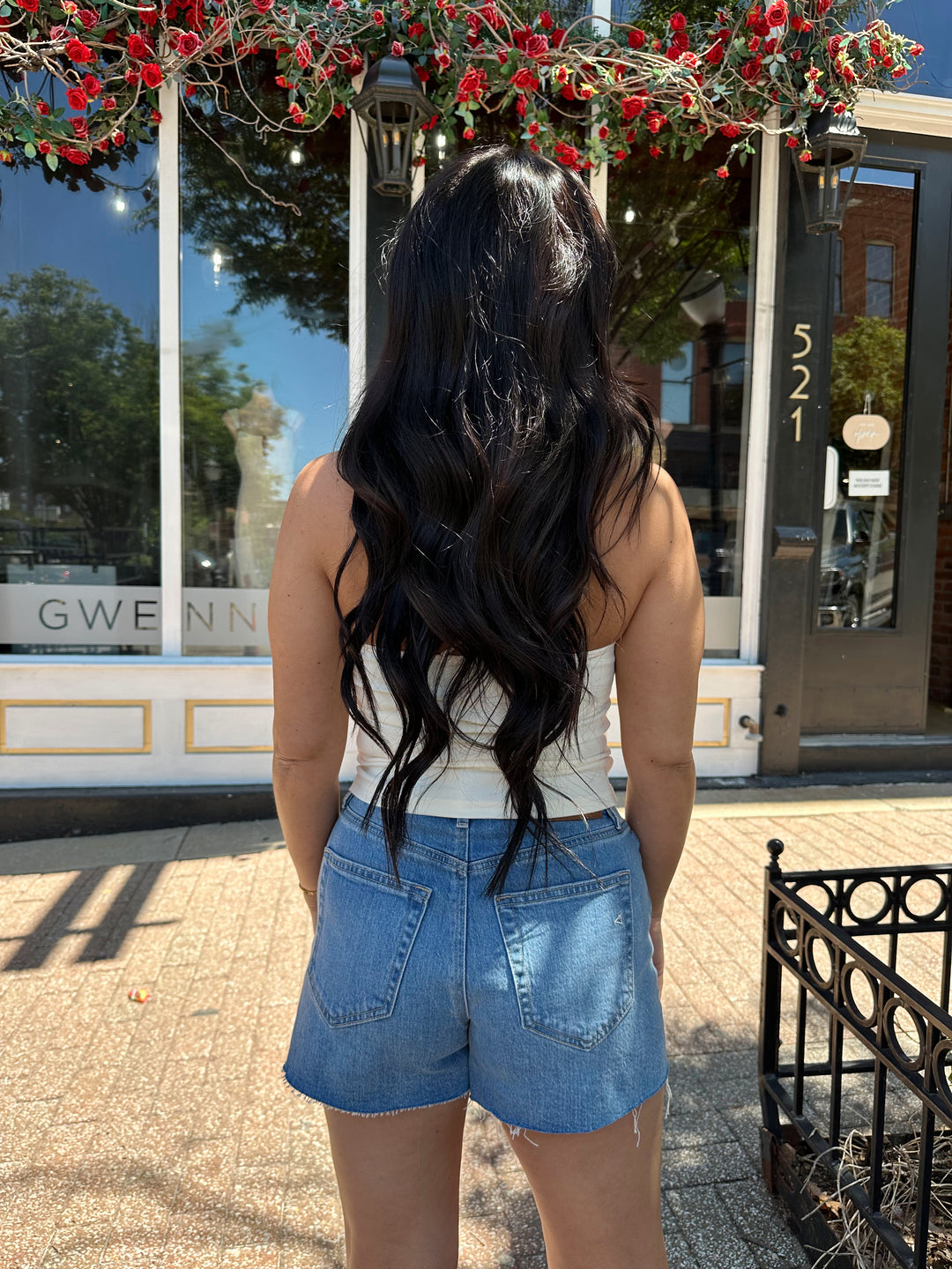 Woman wearing cream colored halter top with beading detail and denim shorts. 