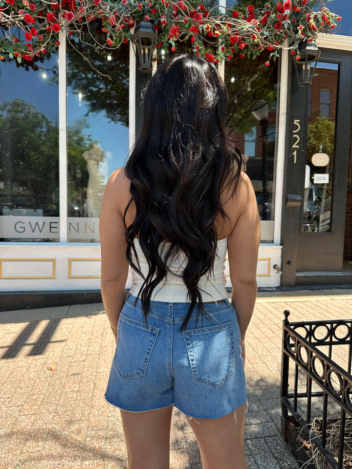 Woman wearing cream colored halter top with beading detail and denim shorts. 