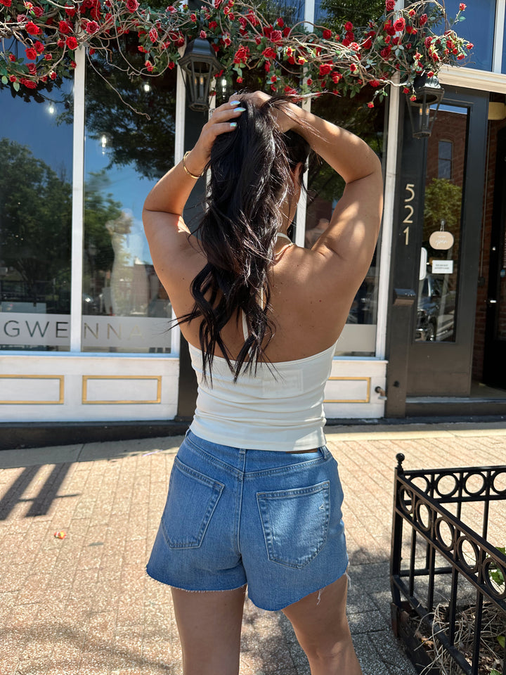 Woman wearing cream colored halter top with beading detail and denim shorts. 