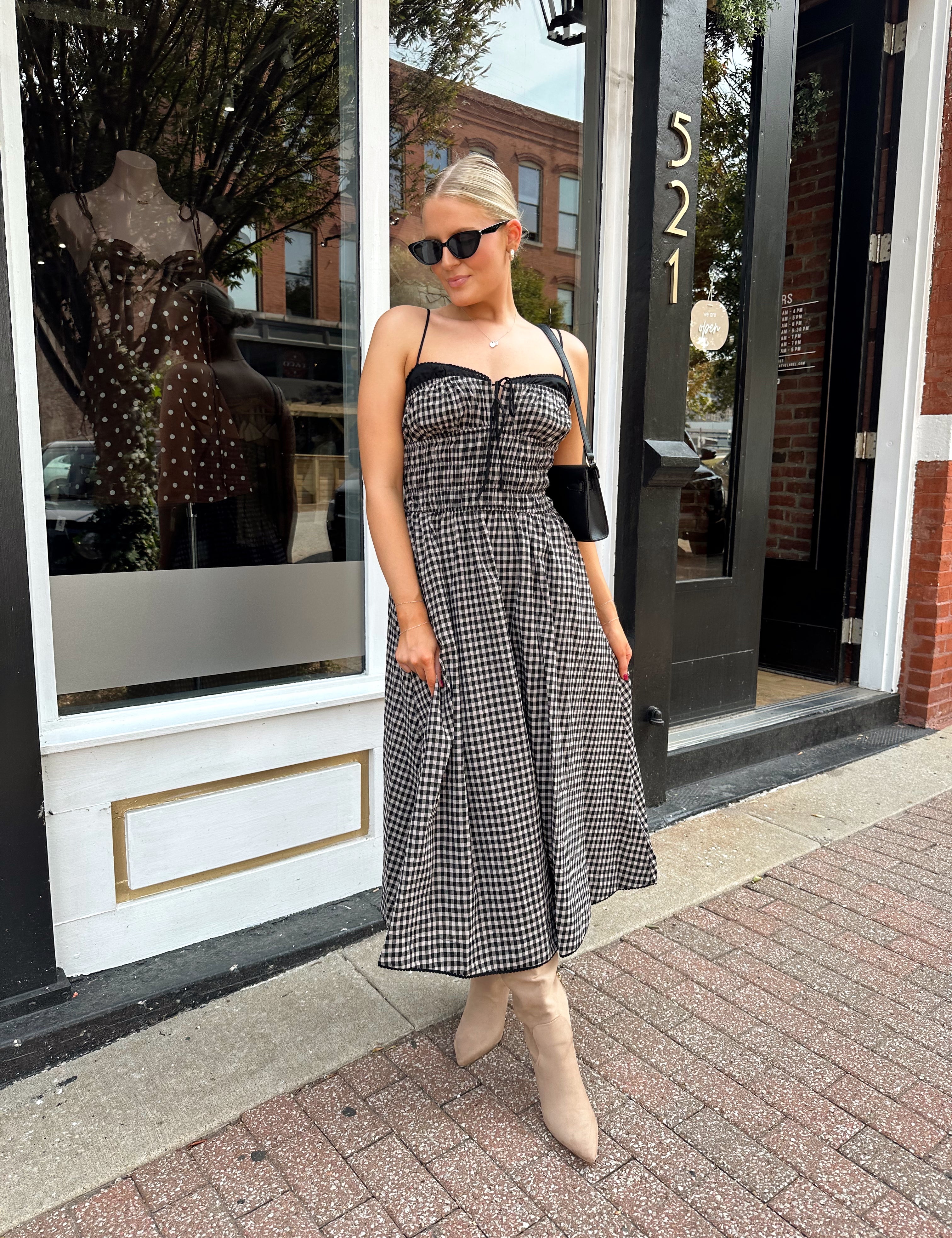 Woman wearing black and taupe plaid midi dress with adjustable straps and knee boots.
