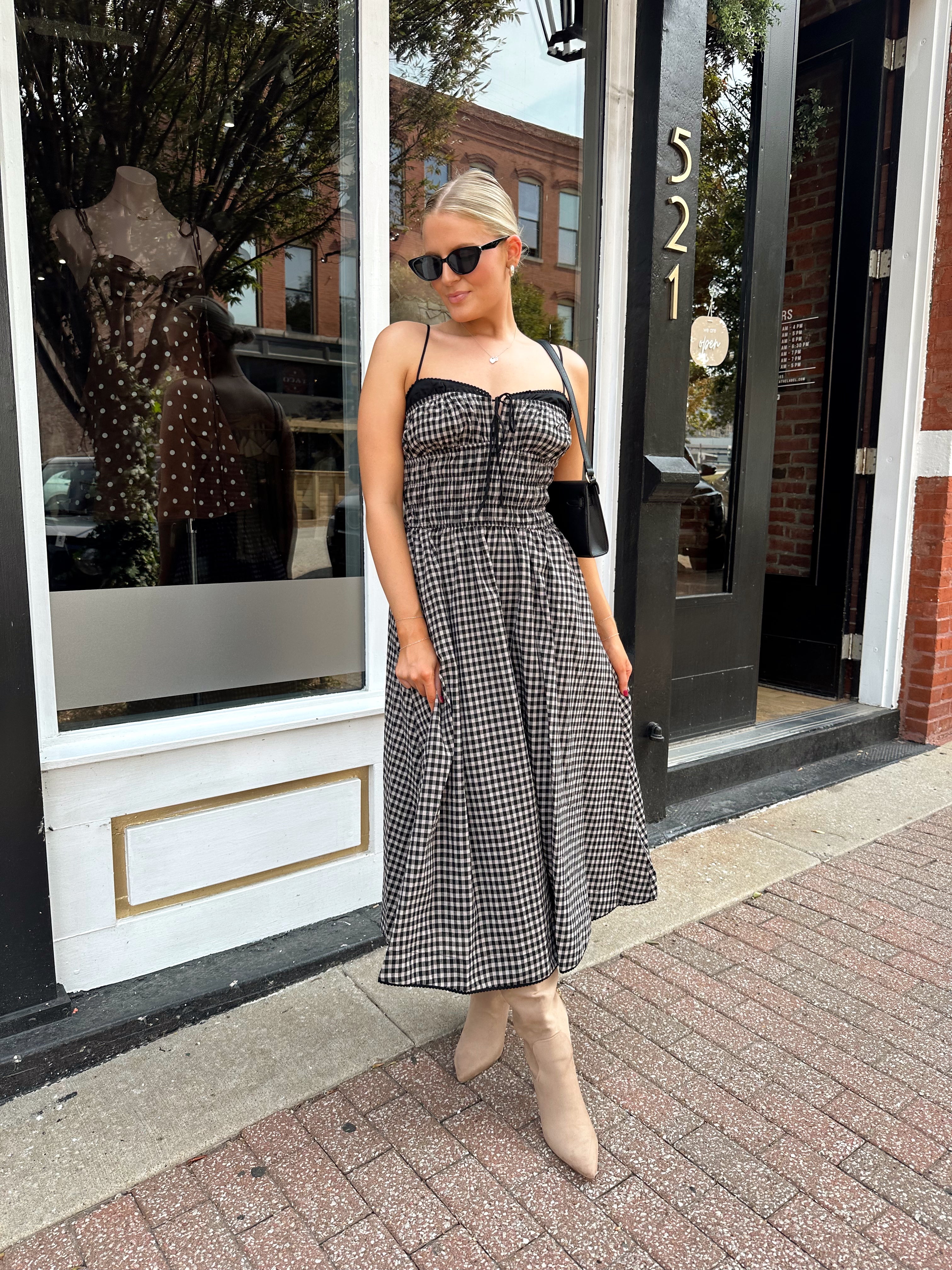 Woman wearing black and taupe plaid midi dress with adjustable straps and knee boots.