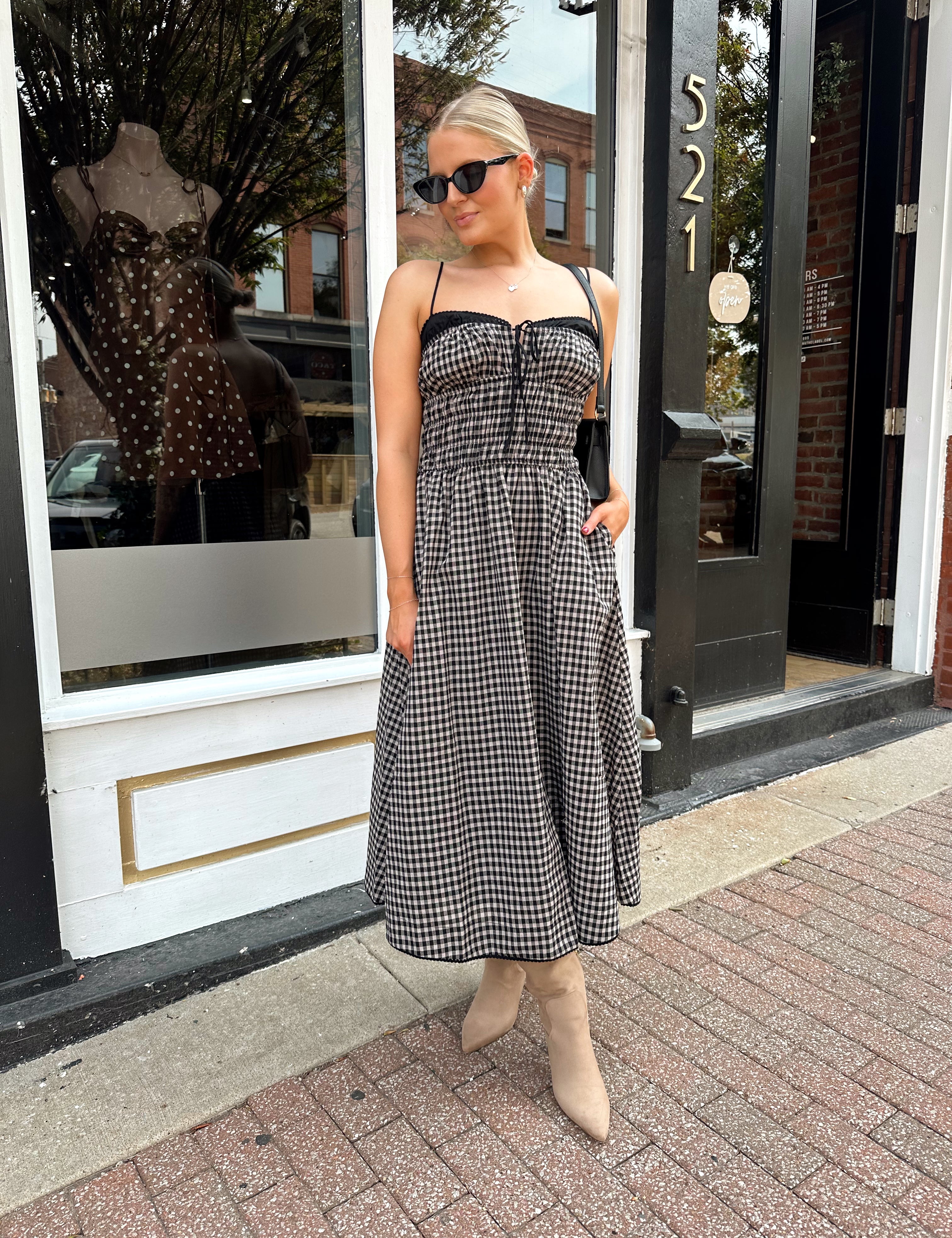 Woman wearing black and taupe plaid midi dress with adjustable straps and knee boots.