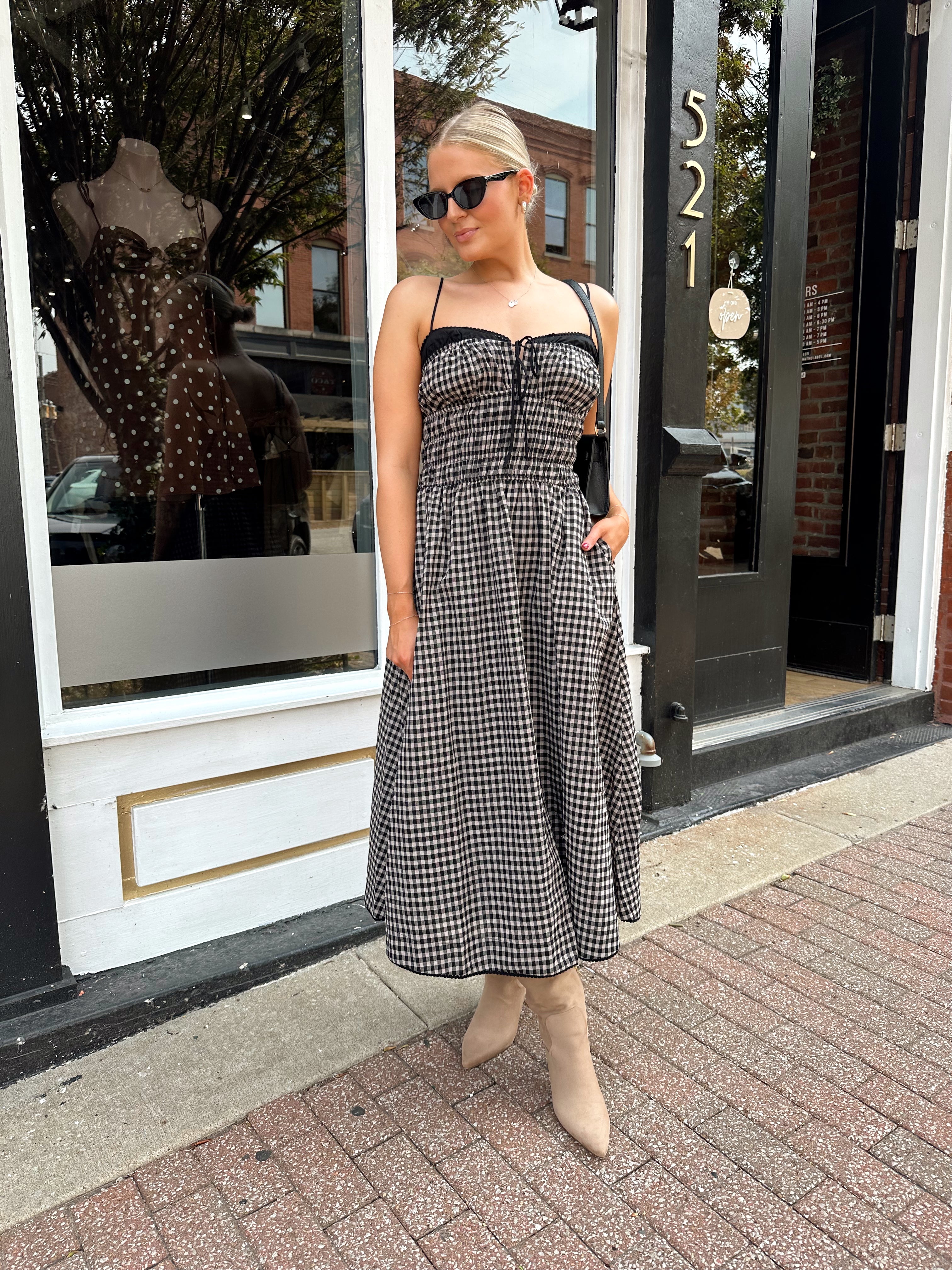 Woman wearing black and taupe plaid midi dress with adjustable straps and knee boots.