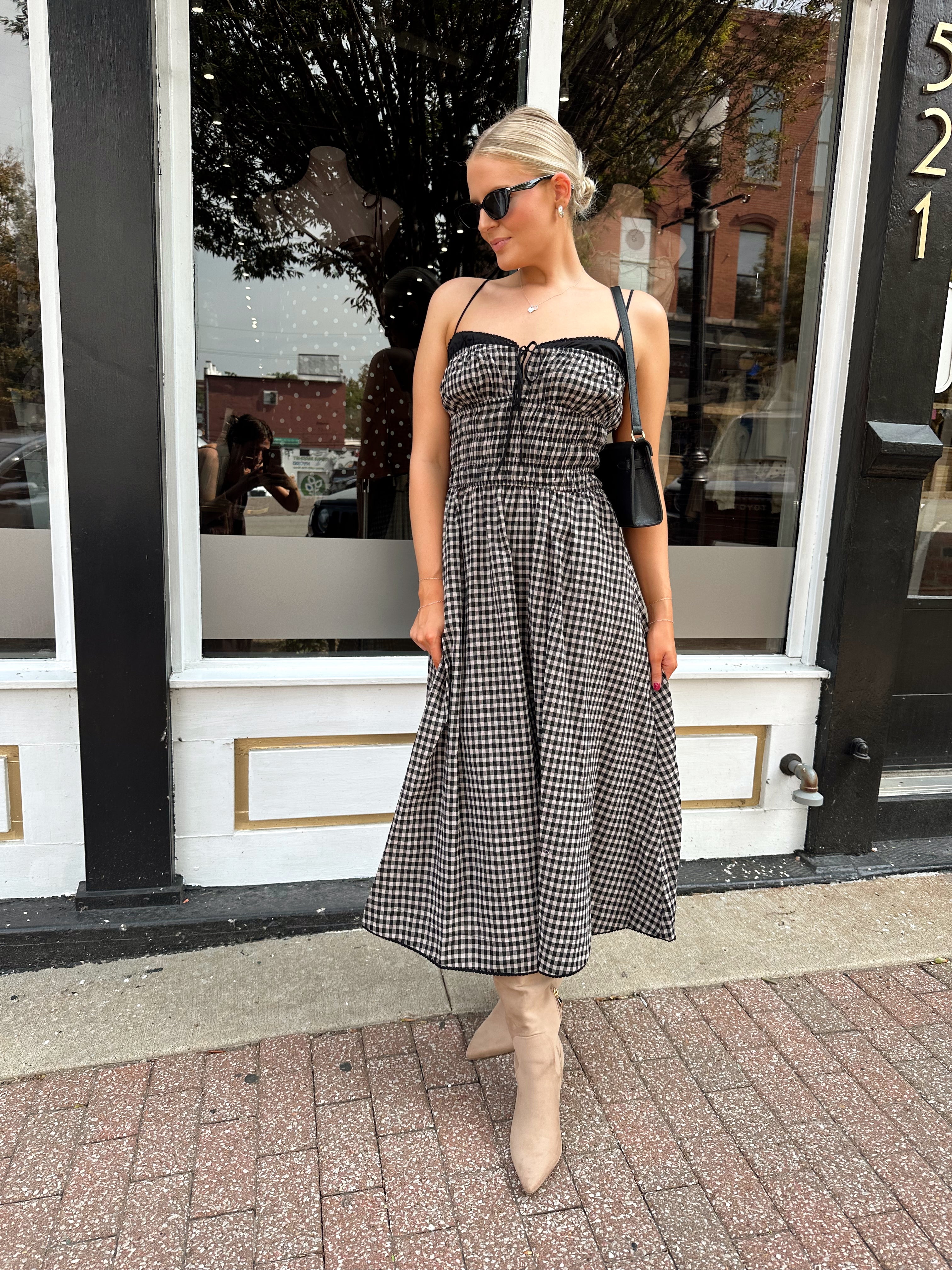 Woman wearing black and taupe plaid midi dress with adjustable straps and knee boots.