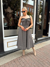 Woman wearing black and taupe plaid midi dress with adjustable straps and knee boots.