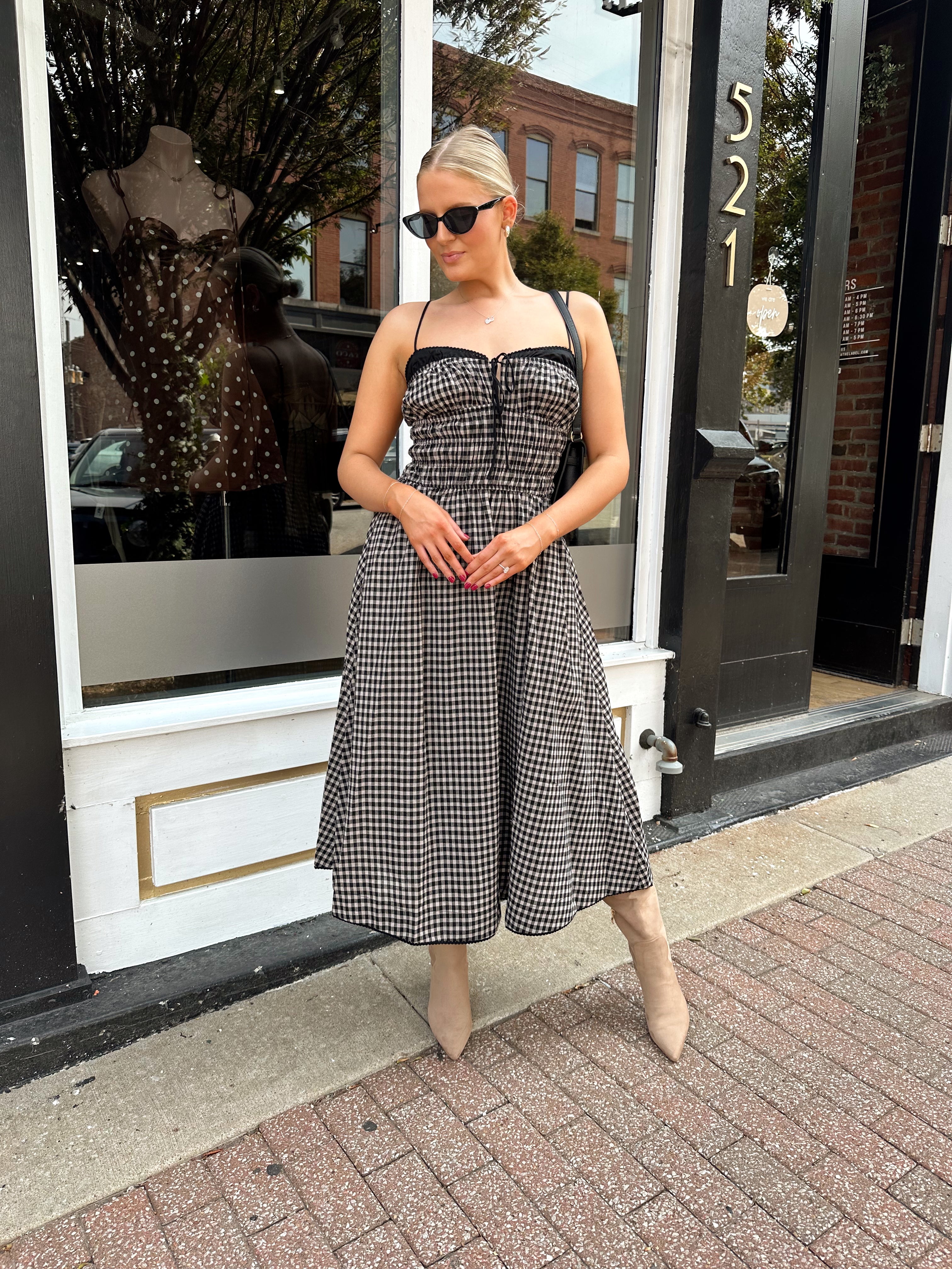 Woman wearing black and taupe plaid midi dress with adjustable straps and knee boots.
