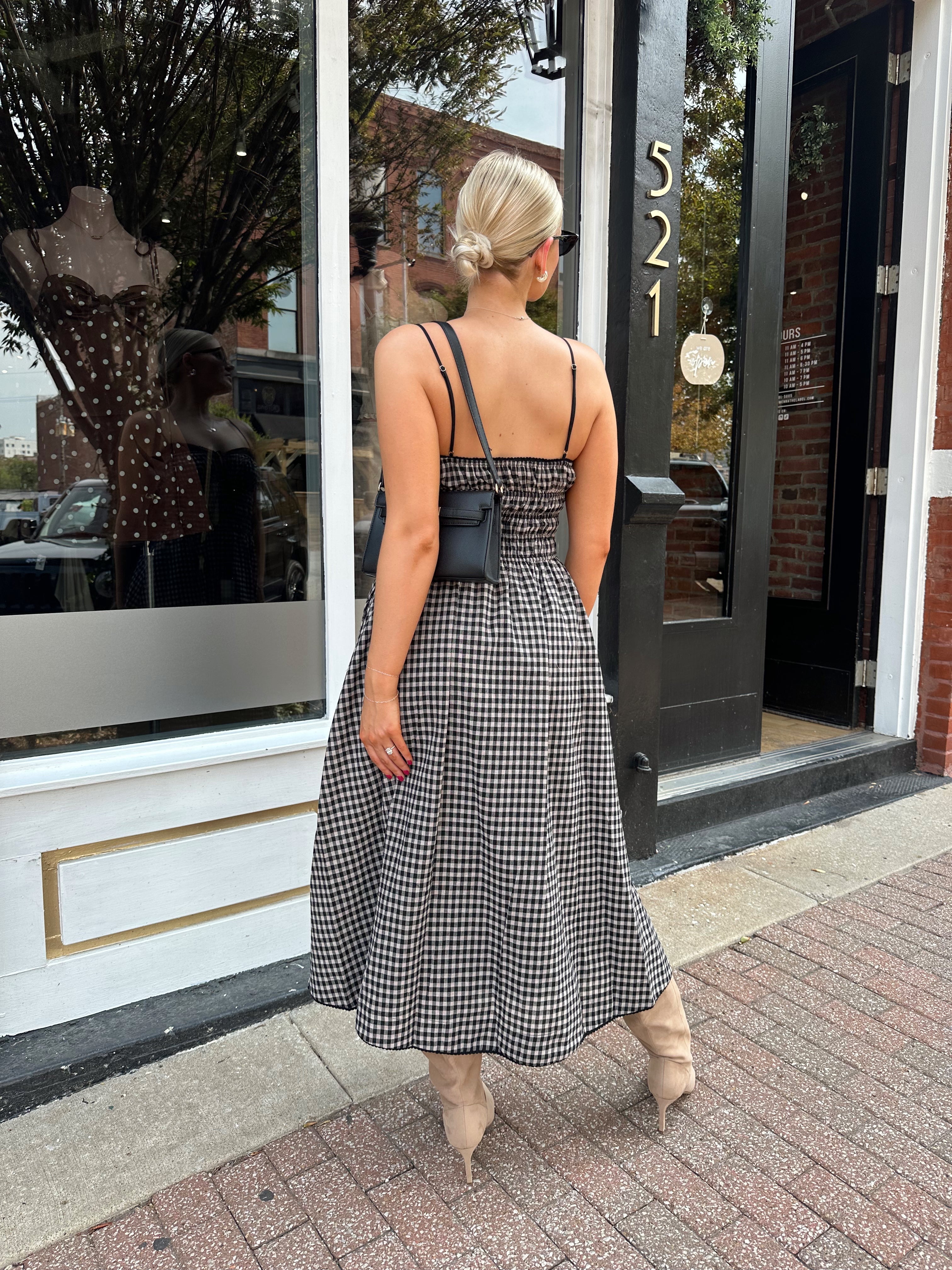 Woman wearing black and taupe plaid midi dress with adjustable straps and knee boots.