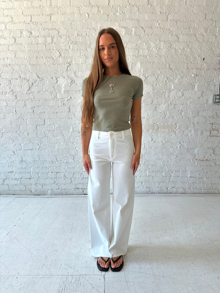Woman wearing green baby tee with beaded detailing and white wide leg jeans.