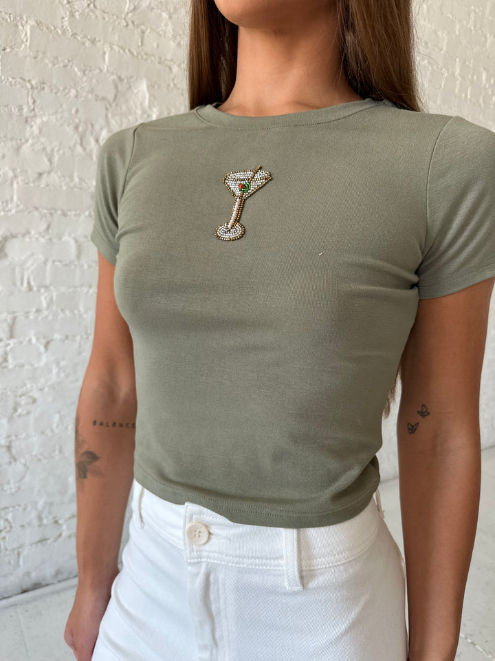 Woman wearing green baby tee with beaded detailing and white wide leg jeans.