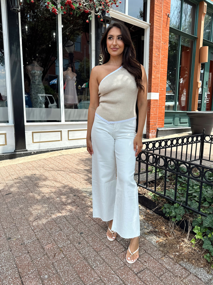 Woman wearing tan knit ribbed one shoulder top with white jeans. 