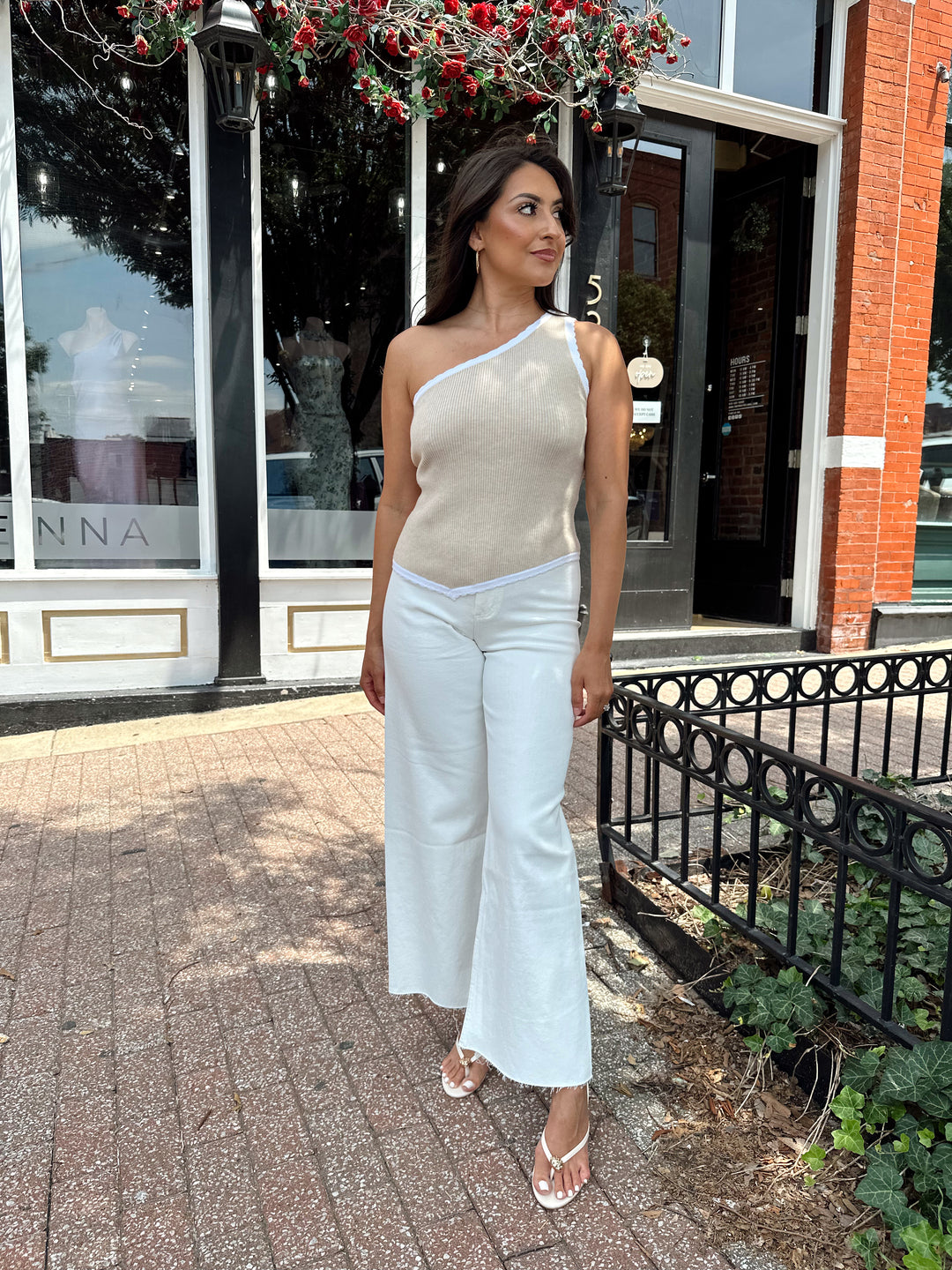 Woman wearing tan knit ribbed one shoulder top with white jeans. 