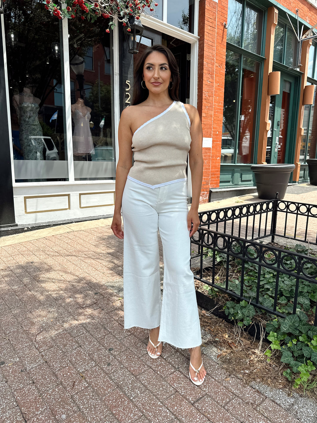 Woman wearing tan knit ribbed one shoulder top with white jeans. 