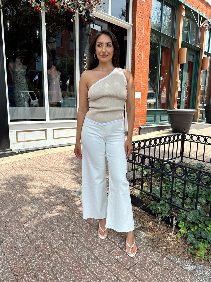 Woman wearing tan knit ribbed one shoulder top with white jeans. 
