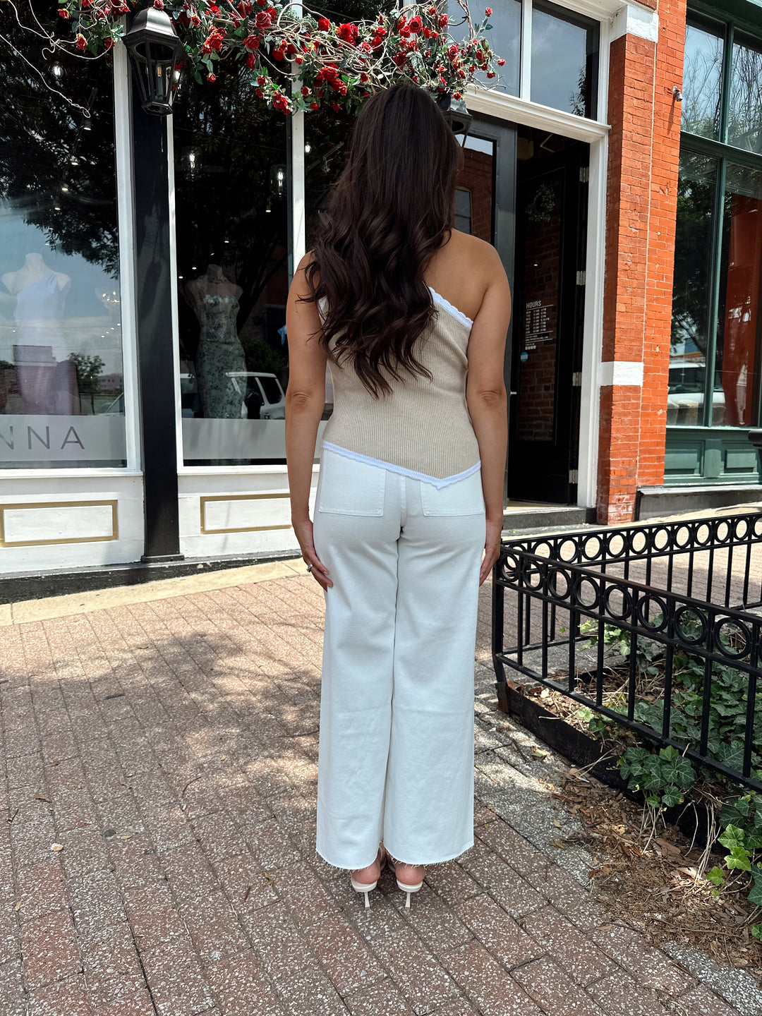Woman wearing tan knit ribbed one shoulder top with white jeans. 