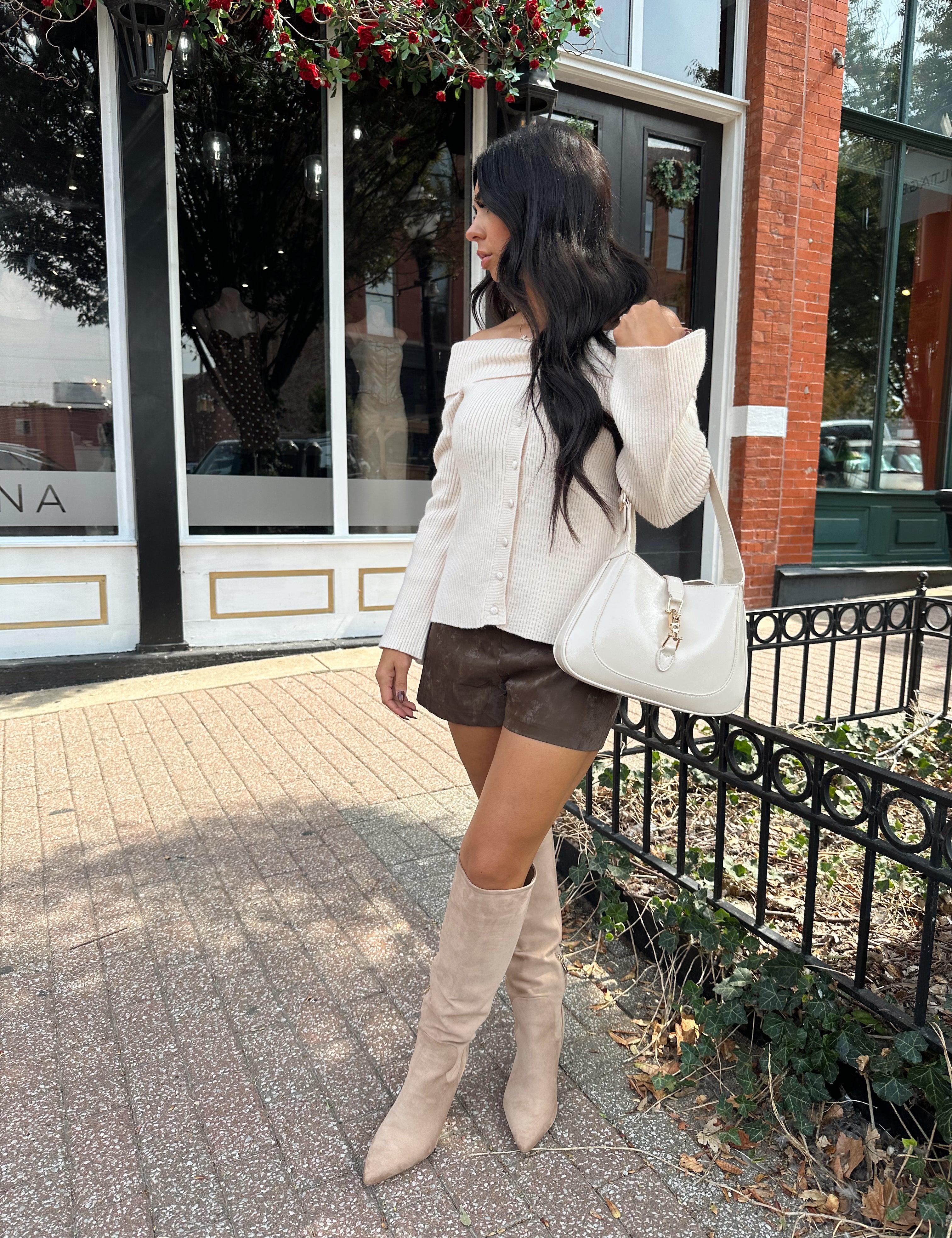 Woman wearing dark brown leather shorts with cream off the shoulder top.