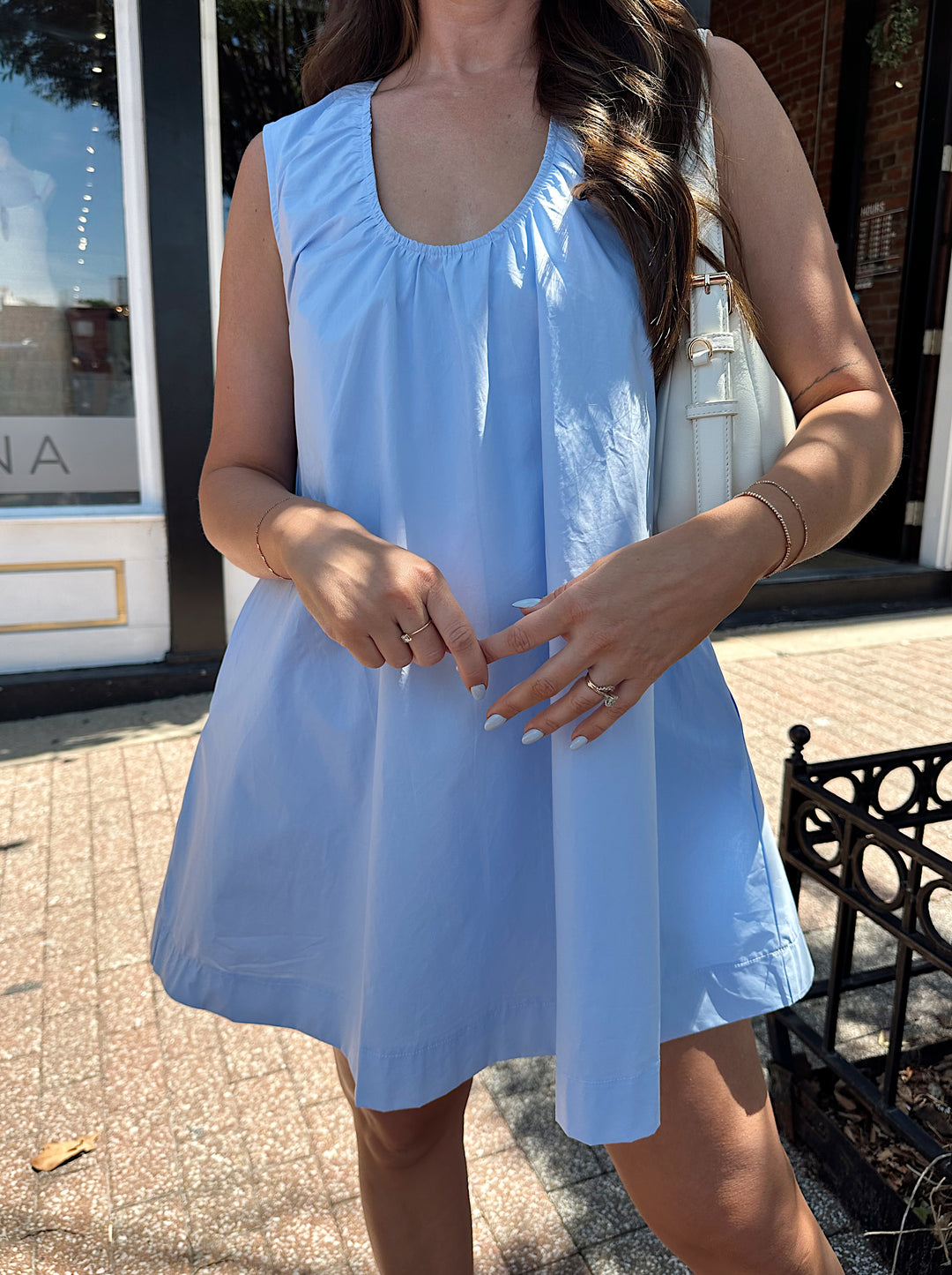 Woman wearing light blue, sleeveless, shift mini dress with gathering detail neckline. 