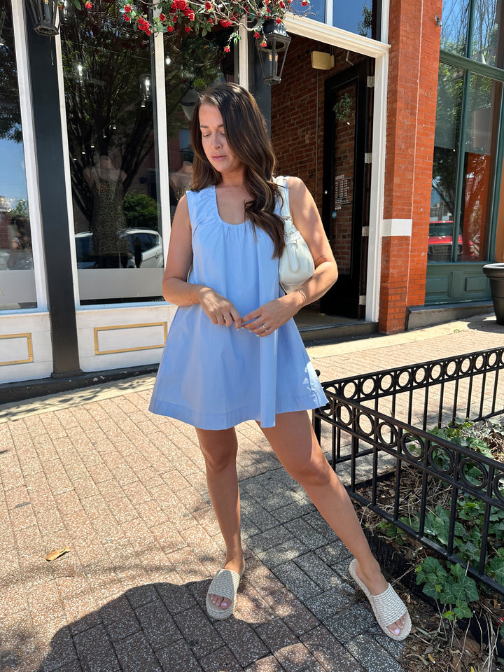 Woman wearing light blue, sleeveless, shift mini dress with gathering detail neckline. 