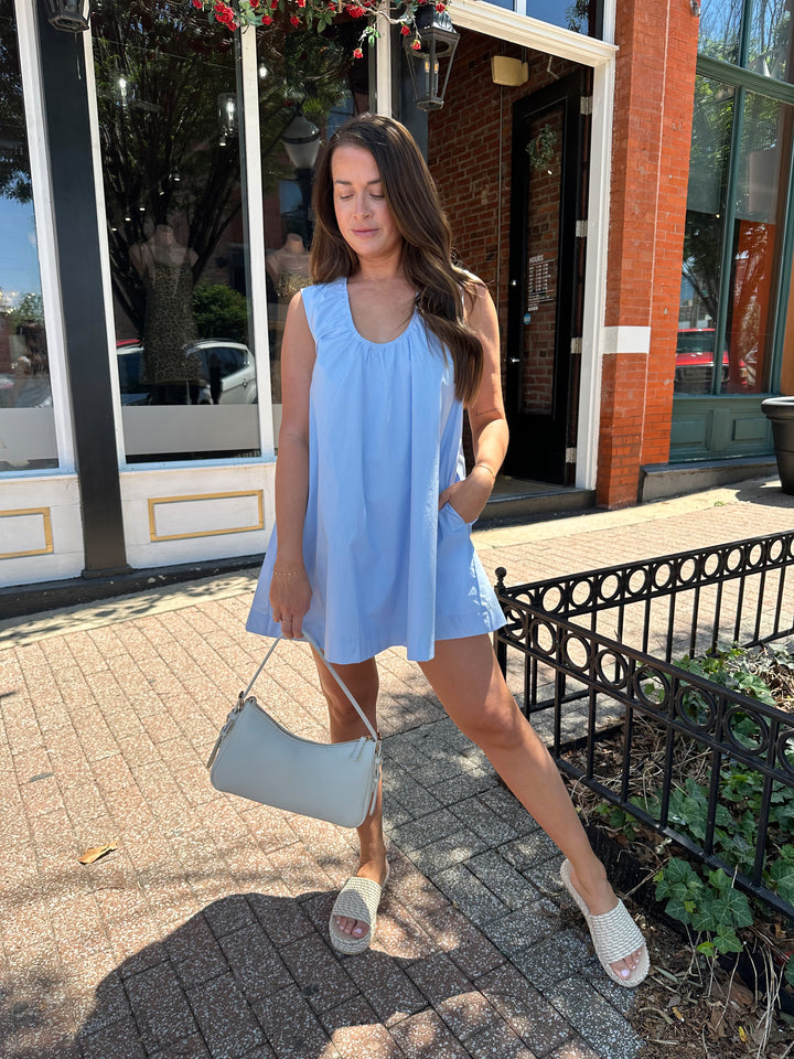 Woman wearing light blue, sleeveless, shift mini dress with gathering detail neckline. 