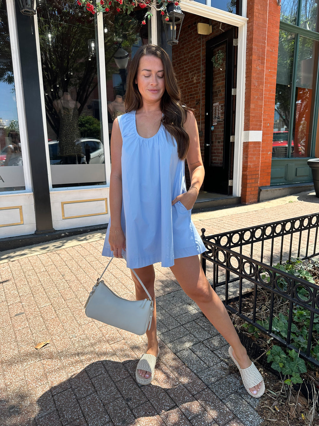 Woman wearing light blue, sleeveless, shift mini dress with gathering detail neckline. 