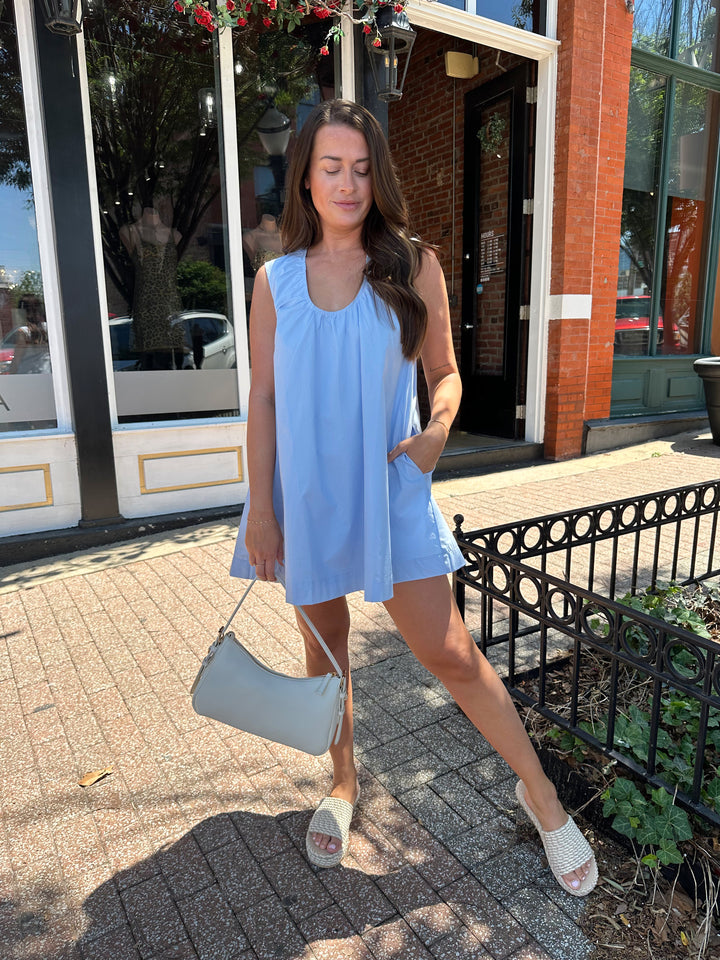 Woman wearing light blue, sleeveless, shift mini dress with gathering detail neckline. 