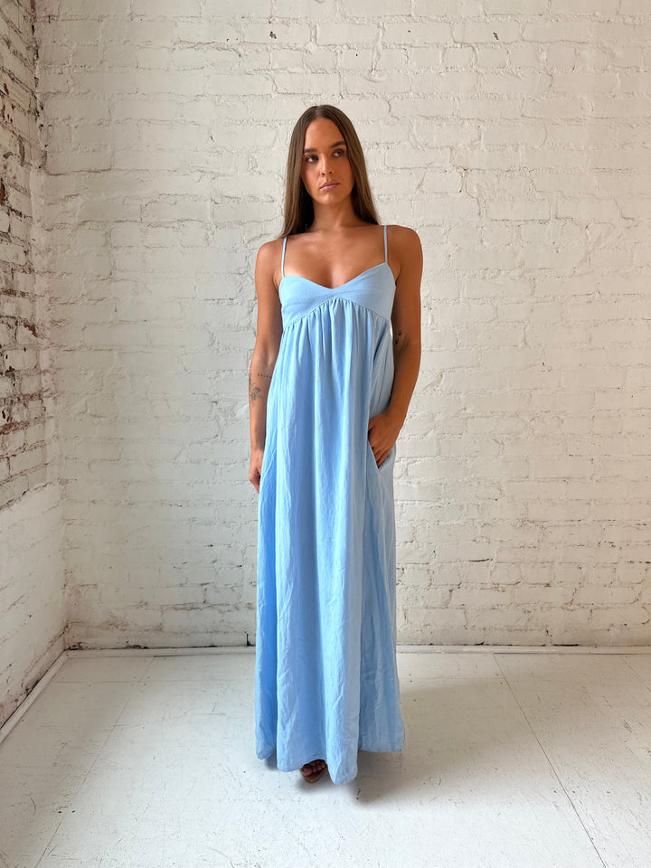 Woman wearing light blue maxi dress with sweetheart neckline, and functional pockets.