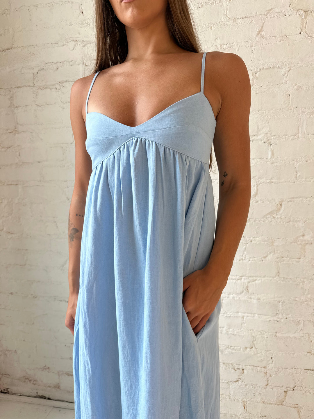 Woman wearing light blue maxi dress with sweetheart neckline, and functional pockets.