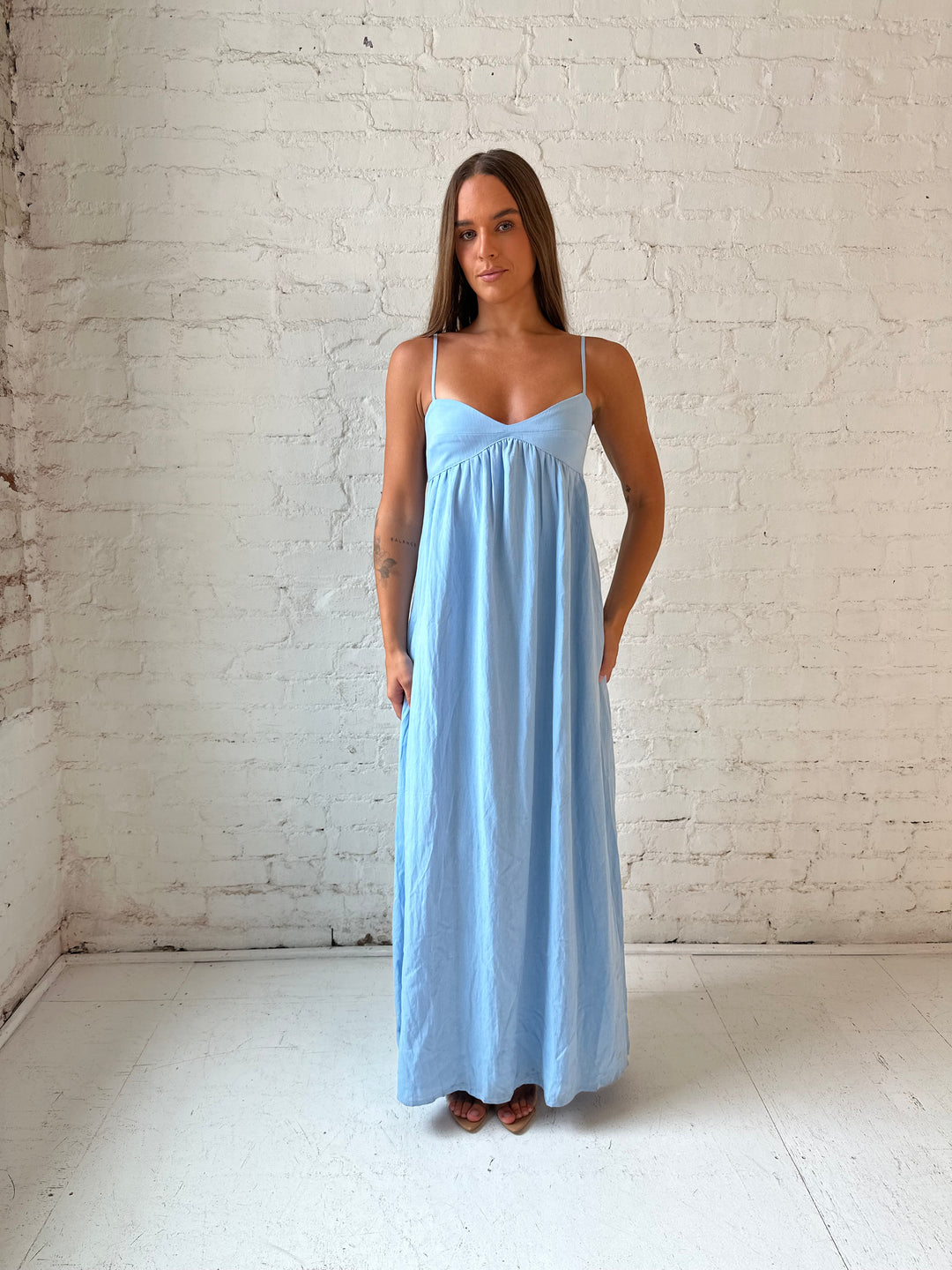 Woman wearing light blue maxi dress with sweetheart neckline, and functional pockets.