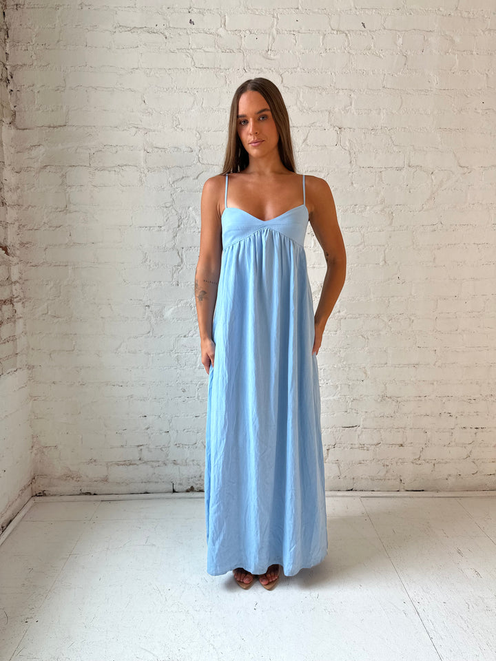 Woman wearing light blue maxi dress with sweetheart neckline, and functional pockets.