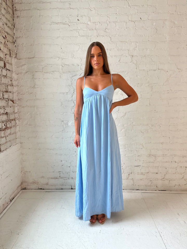 Woman wearing light blue maxi dress with sweetheart neckline, and functional pockets.