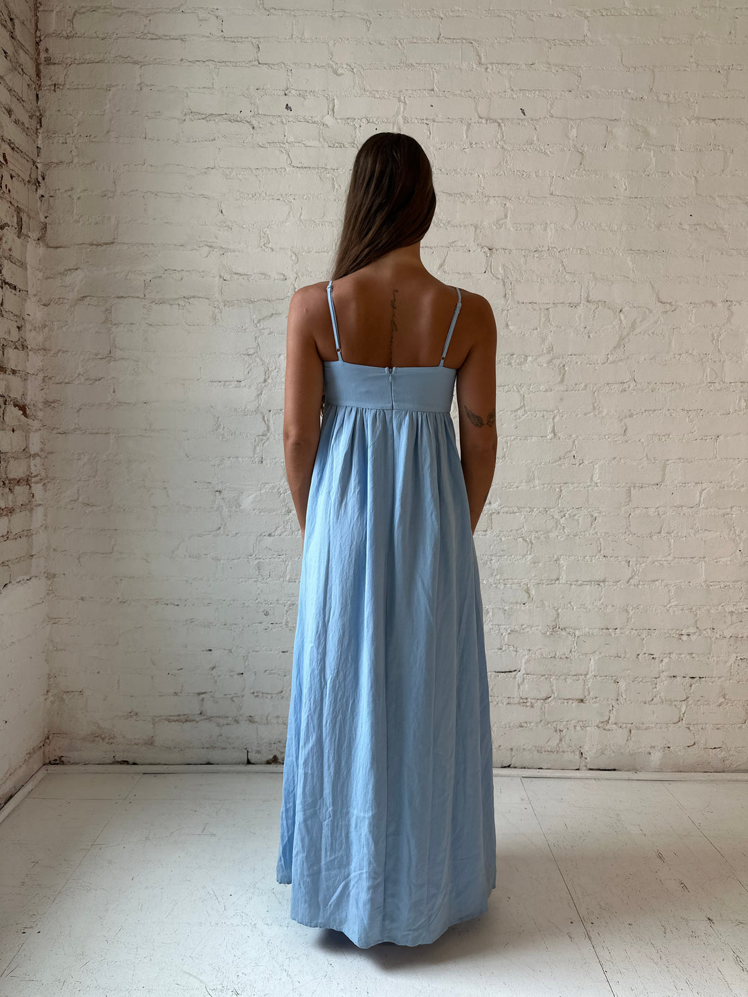 Woman wearing light blue maxi dress with sweetheart neckline, and functional pockets.