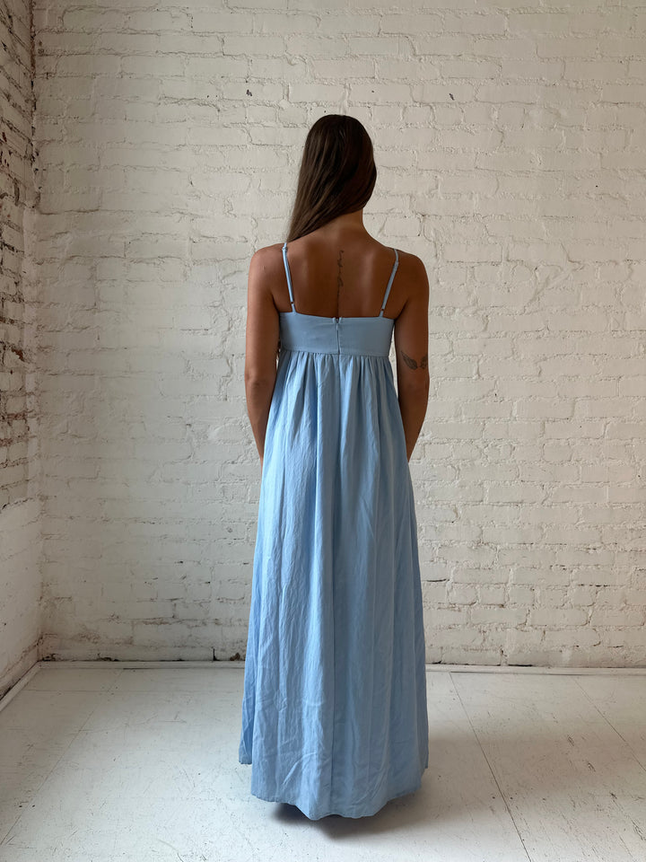 Woman wearing light blue maxi dress with sweetheart neckline, and functional pockets.