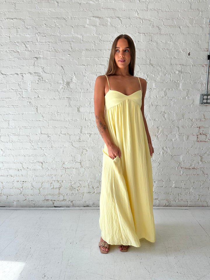 Woman wearing yellow maxi dress with sweetheart neckline, functional pockets, and adjustable straps.
