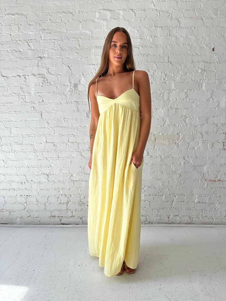 Woman wearing yellow maxi dress with sweetheart neckline, functional pockets, and adjustable straps.