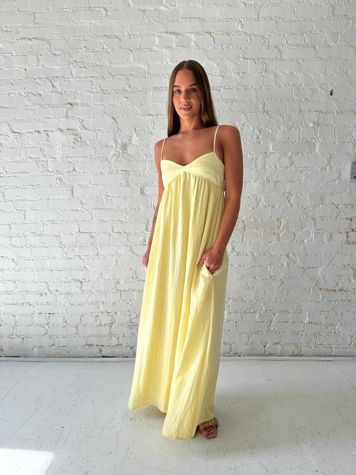 Woman wearing yellow maxi dress with sweetheart neckline, functional pockets, and adjustable straps.
