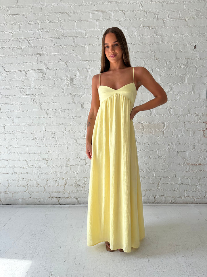 Woman wearing yellow maxi dress with sweetheart neckline, functional pockets, and adjustable straps.