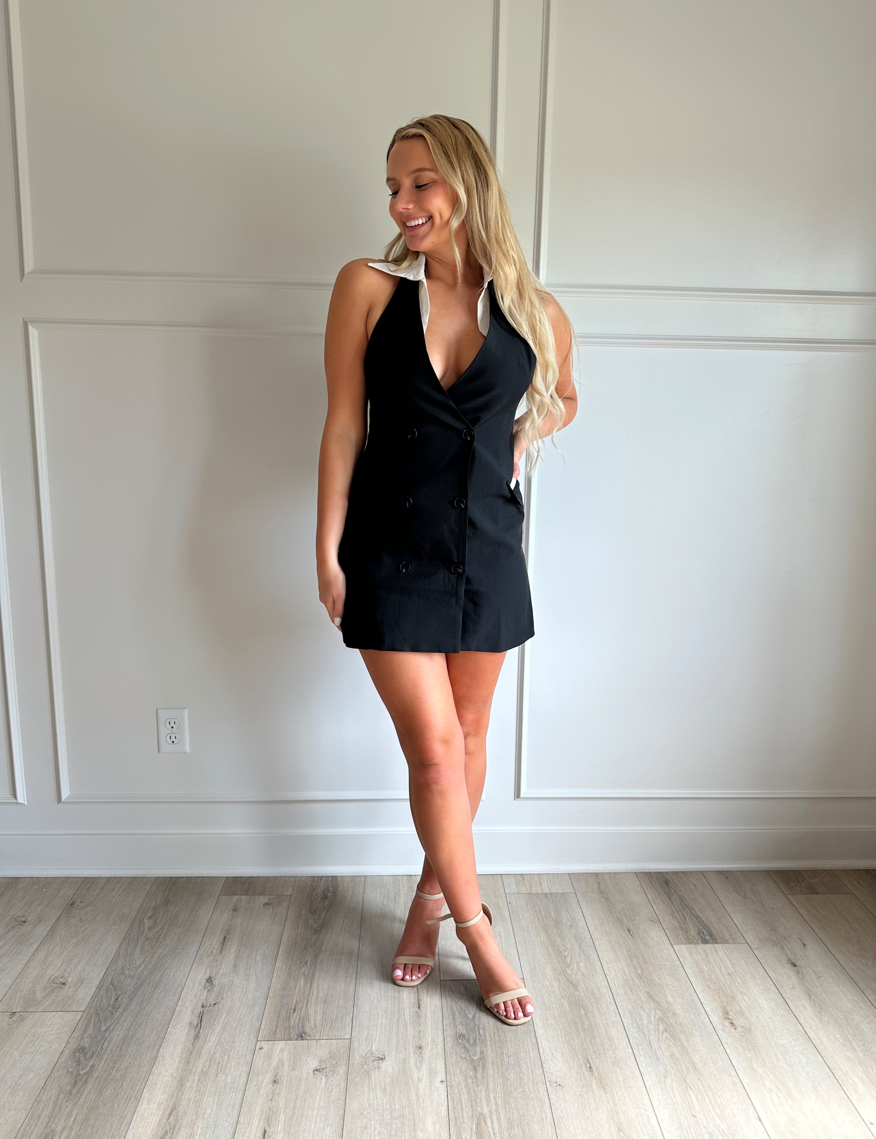 Woman wearing a black tailored mini dress with white collar detailing.