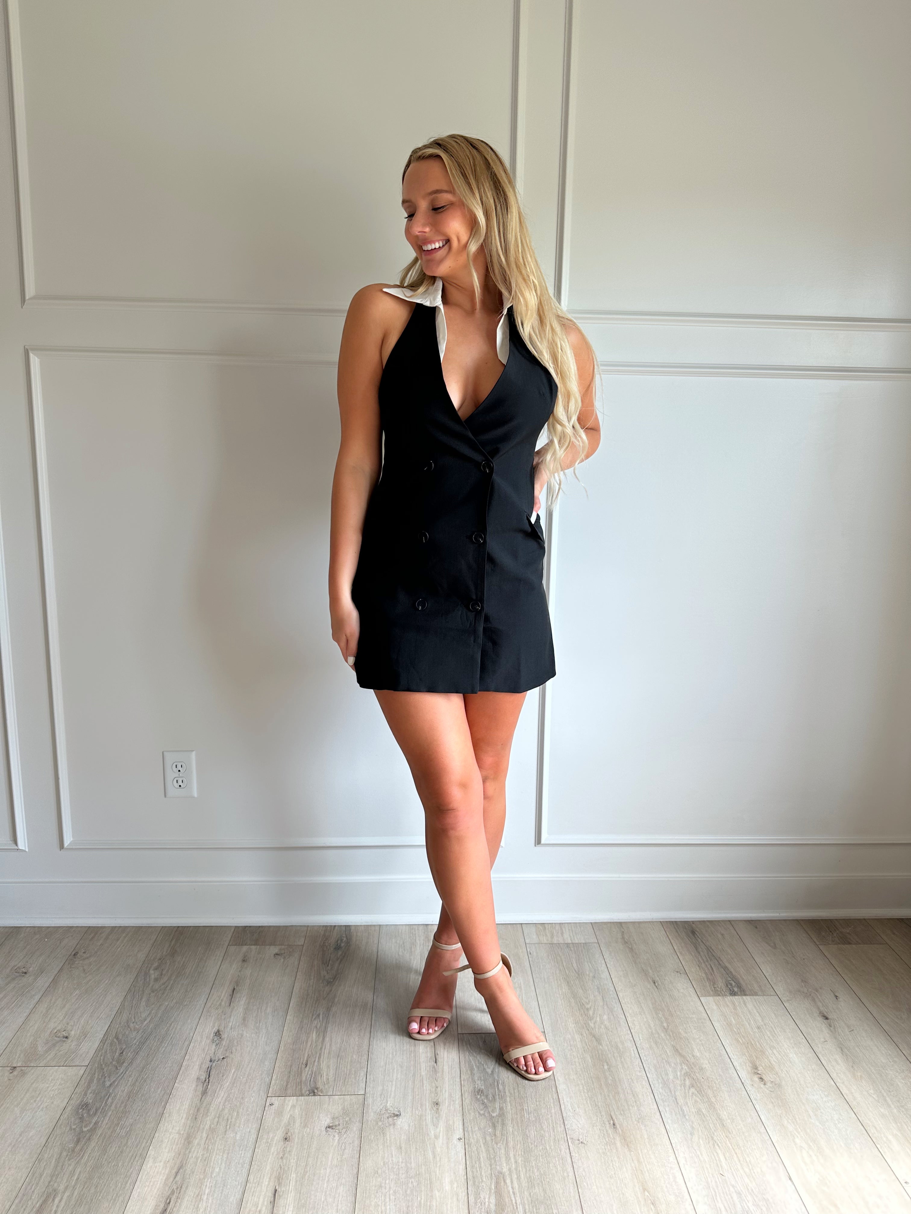 Woman wearing a black tailored mini dress with white collar detailing.