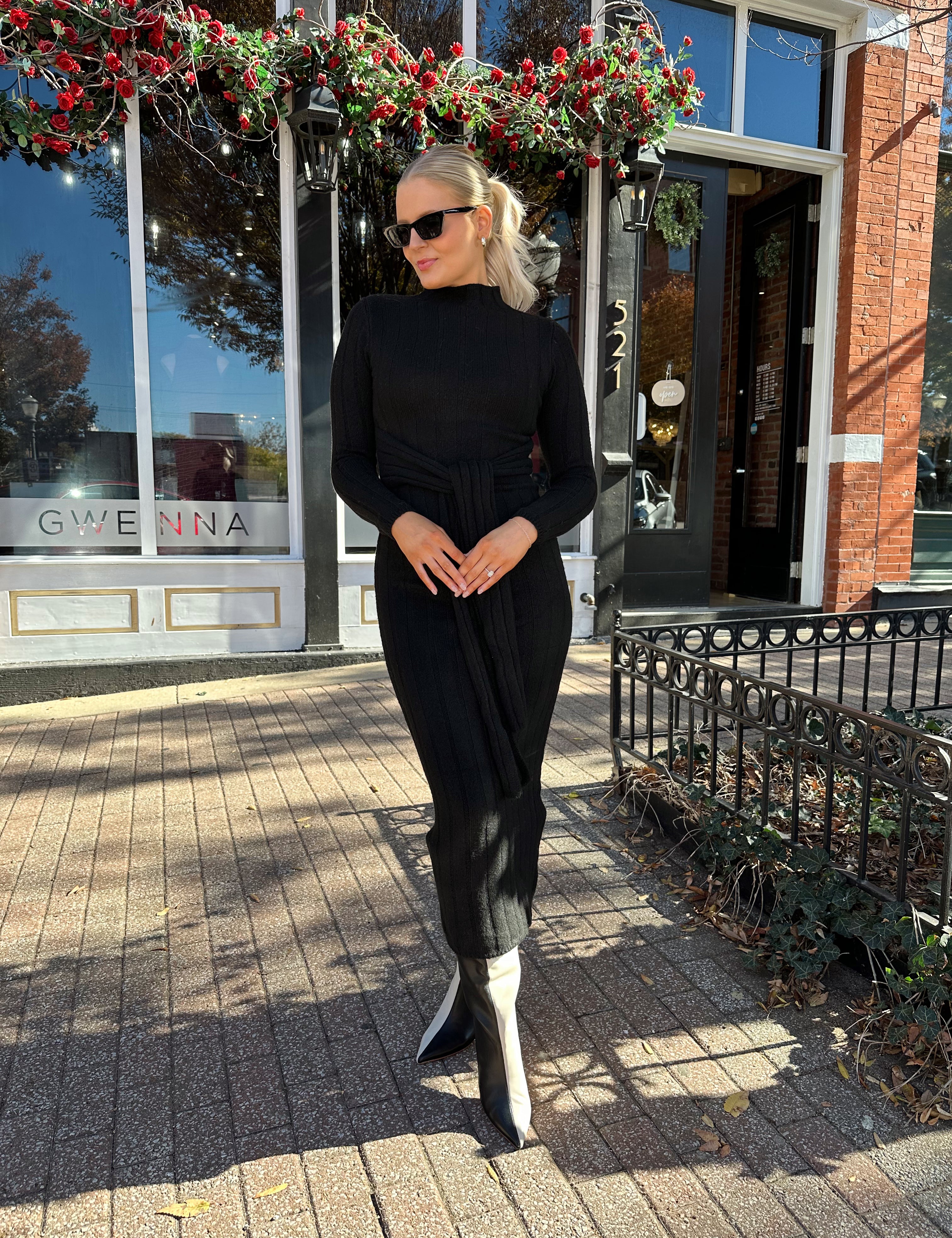 Woman wearing black knit sweater midi dress with front tie detail. 