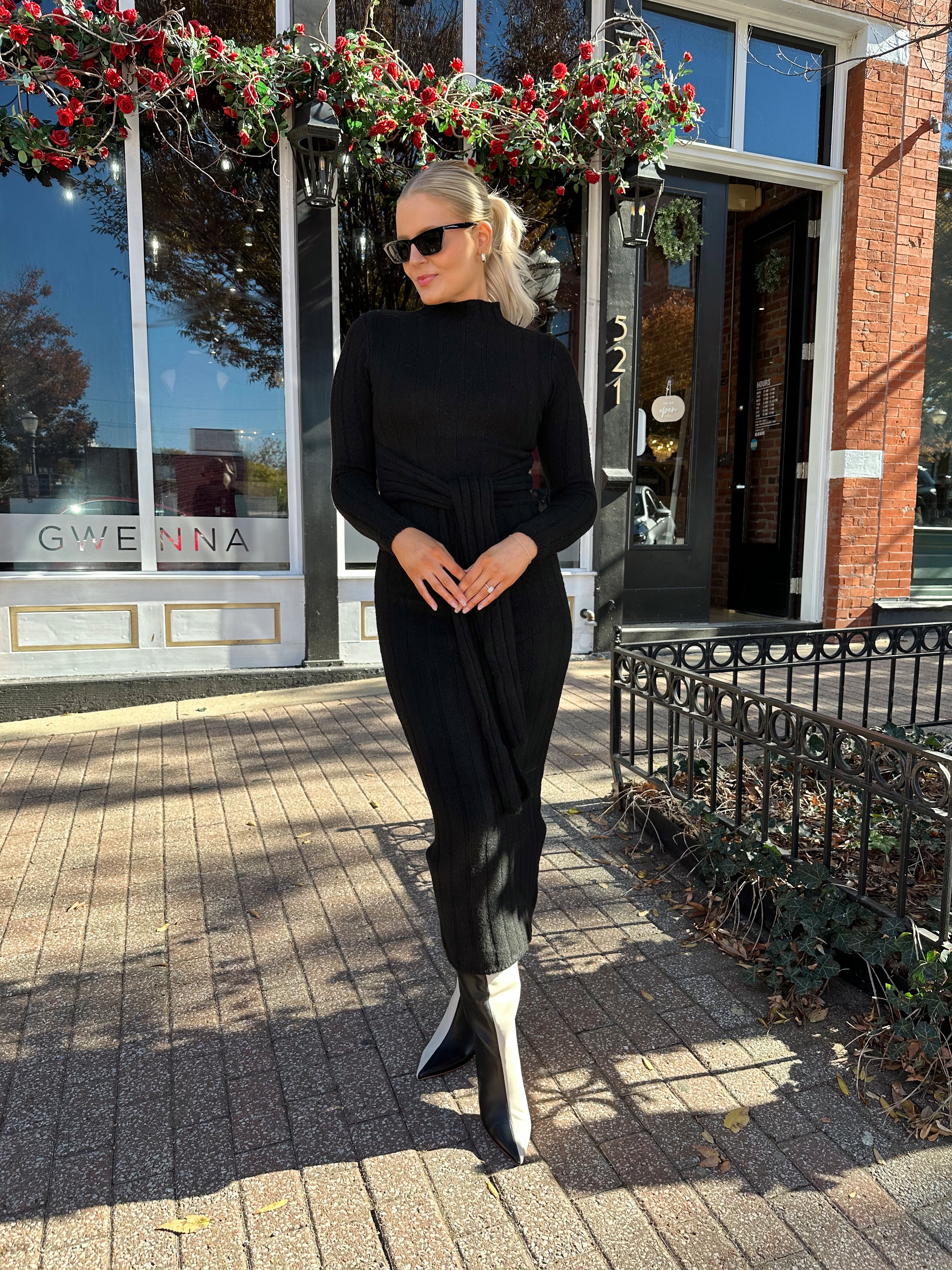 Woman wearing black knit sweater midi dress with front tie detail. 
